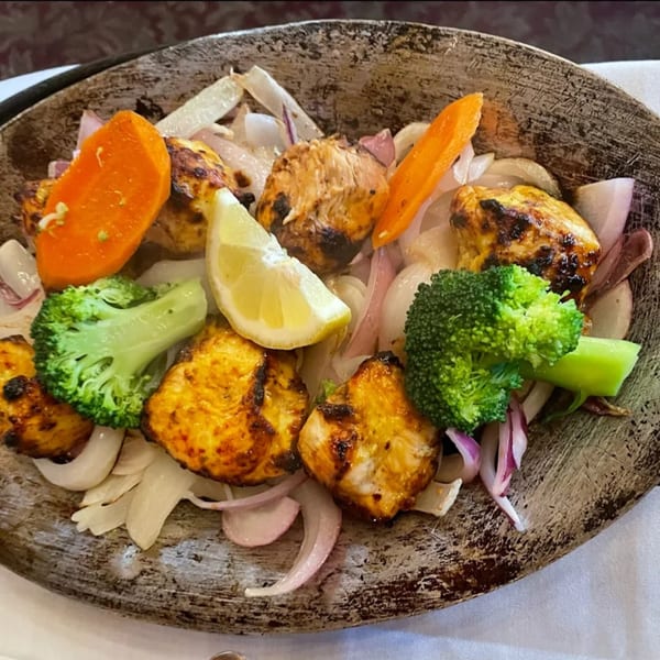 Indian House's chicken tikka with broccoli, carrots, onions, and a lemon wedge on a sizzling platter.